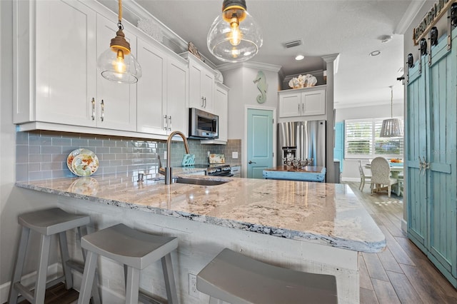 kitchen with a barn door, white cabinetry, hanging light fixtures, and appliances with stainless steel finishes