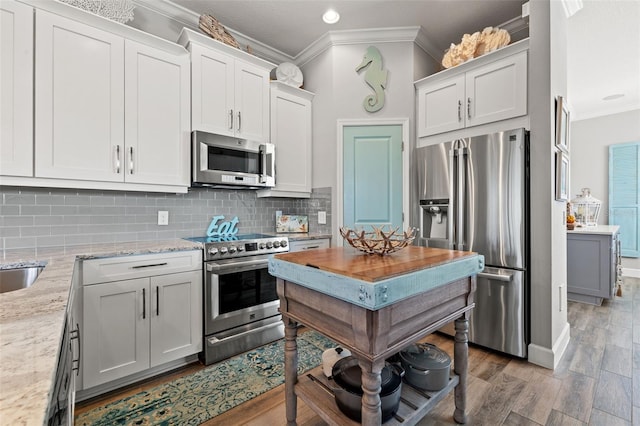 kitchen featuring white cabinetry, light stone counters, crown molding, wood-type flooring, and appliances with stainless steel finishes