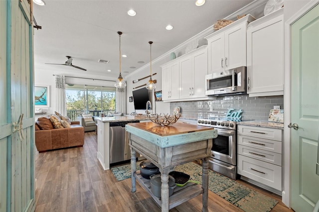 kitchen featuring dark wood-type flooring, appliances with stainless steel finishes, pendant lighting, white cabinets, and ornamental molding