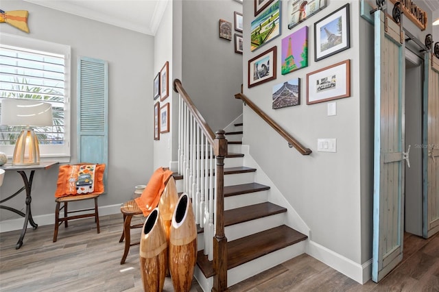 stairway with wood-type flooring, a barn door, and crown molding