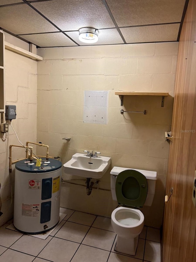 bathroom featuring toilet, a drop ceiling, tile patterned floors, sink, and water heater