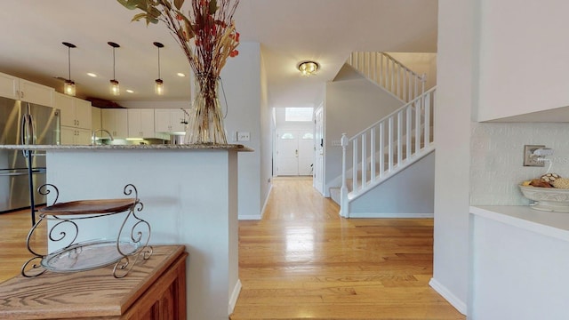 kitchen with white cabinets, light wood-type flooring, decorative light fixtures, and stainless steel refrigerator