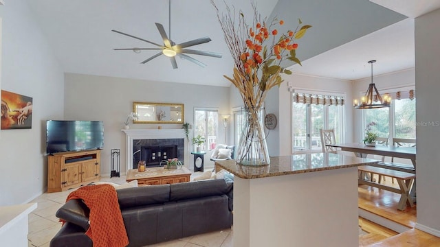 tiled living room with ceiling fan with notable chandelier and a high end fireplace