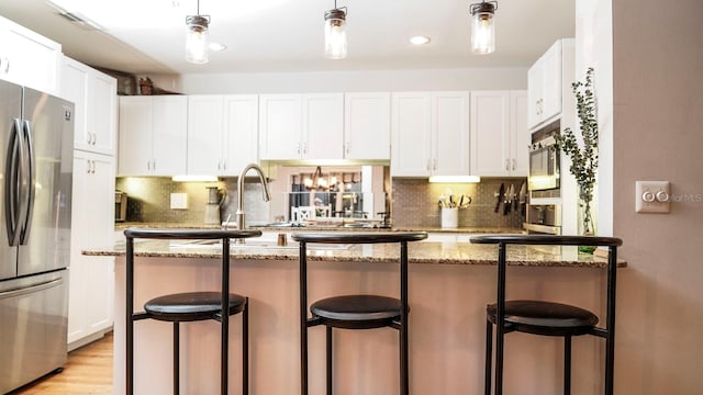 kitchen featuring a kitchen bar, stainless steel refrigerator, white cabinetry, and dark stone counters