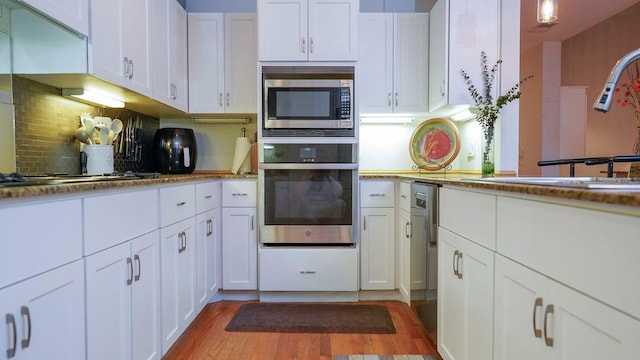 kitchen with tasteful backsplash, stainless steel appliances, sink, light hardwood / wood-style flooring, and white cabinetry