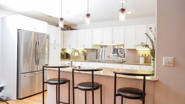 kitchen with stainless steel fridge, white cabinetry, and a breakfast bar area