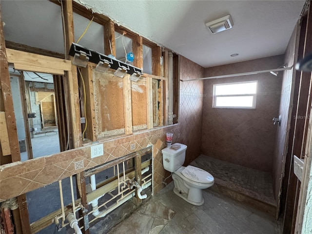 bathroom featuring a tile shower, toilet, and tile walls