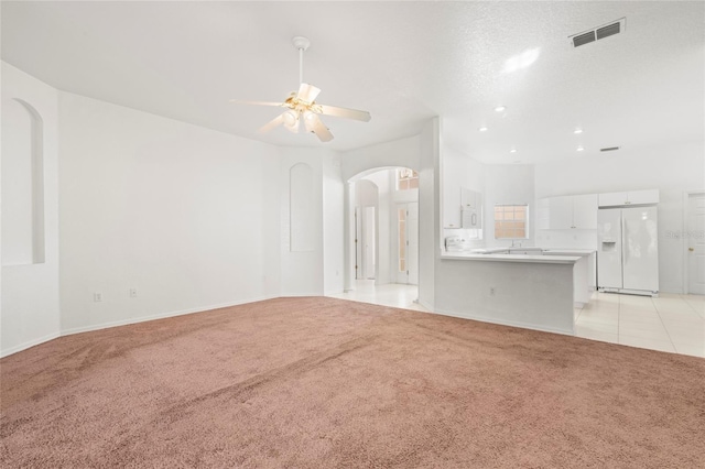 unfurnished living room with ceiling fan, light colored carpet, and a textured ceiling