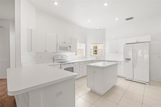 kitchen with white cabinets, light tile patterned floors, a kitchen island, and white appliances