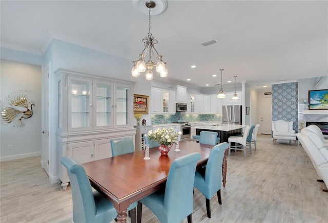 dining room featuring a premium fireplace, an inviting chandelier, ornamental molding, and light wood-type flooring