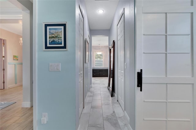 hallway with a chandelier, crown molding, and light hardwood / wood-style floors