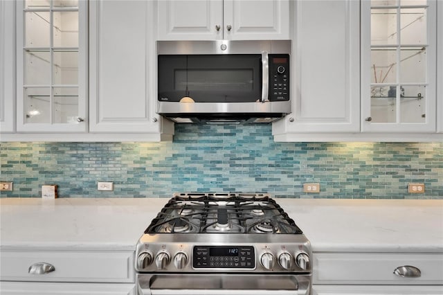 721 Manns Harbor Dr, Apollo Beach, FL 33572 - kitchen featuring stainless steel appliances, white cabinetry, glass insert cabinets, and decorative backsplash