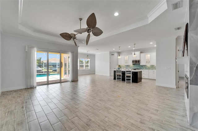 721 Manns Harbor Dr, Apollo Beach, FL 33572 - unfurnished living room with a tray ceiling, ceiling fan, ornamental molding, recessed lighting, and light wood-style flooring