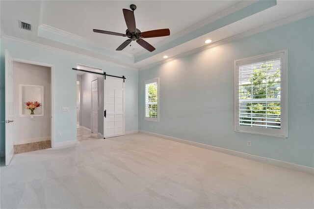 721 Manns Harbor Dr, Apollo Beach, FL 33572 - unfurnished bedroom with ornamental molding, a tray ceiling, a barn door, carpet flooring, and ceiling fan