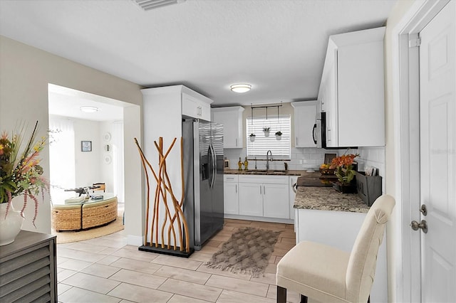 kitchen featuring decorative backsplash, appliances with stainless steel finishes, dark stone counters, sink, and white cabinetry