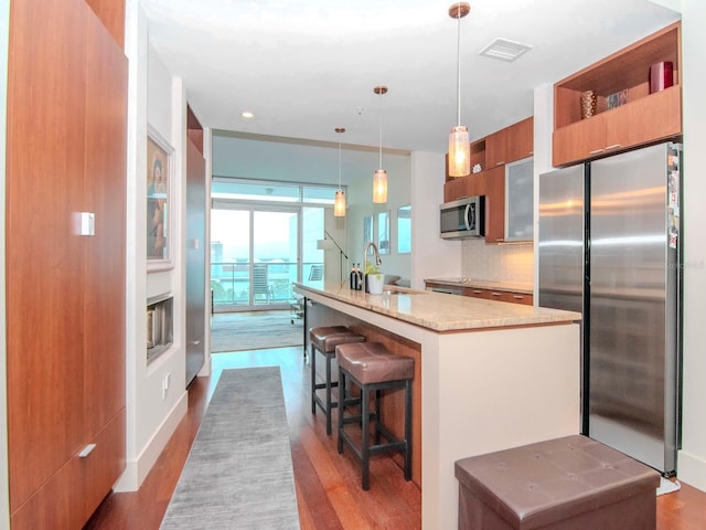 kitchen featuring tasteful backsplash, light stone counters, stainless steel appliances, hardwood / wood-style floors, and hanging light fixtures