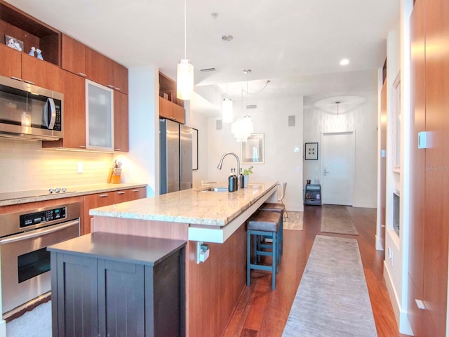 kitchen featuring sink, dark hardwood / wood-style flooring, a kitchen island with sink, a breakfast bar, and appliances with stainless steel finishes