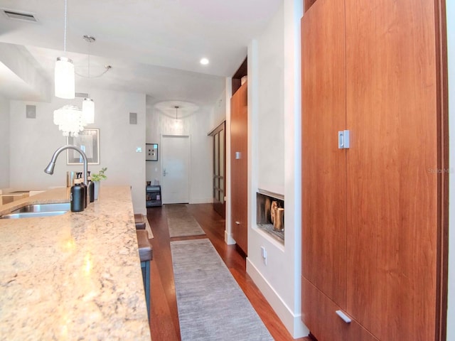 kitchen with light stone counters, sink, wood-type flooring, decorative light fixtures, and a chandelier