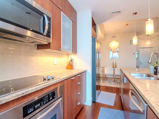 kitchen featuring pendant lighting, dark wood-type flooring, sink, light stone countertops, and stainless steel appliances