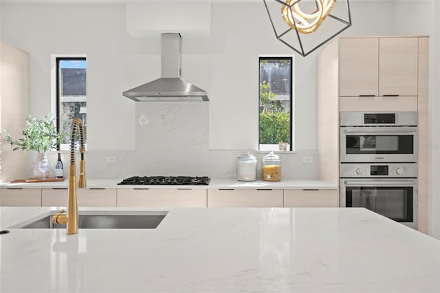 kitchen featuring pendant lighting, sink, wall chimney exhaust hood, light stone countertops, and appliances with stainless steel finishes