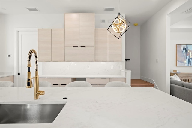 kitchen featuring light stone countertops, hardwood / wood-style flooring, hanging light fixtures, and sink