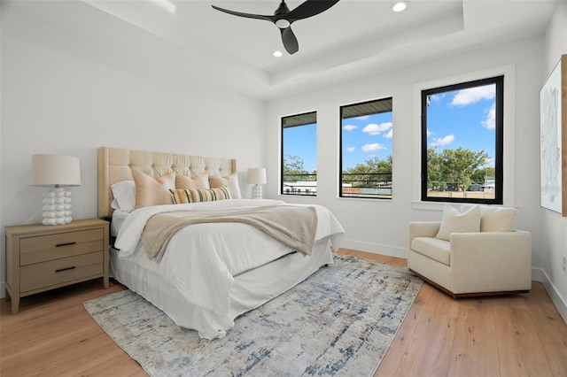 bedroom with ceiling fan, light hardwood / wood-style flooring, and a tray ceiling