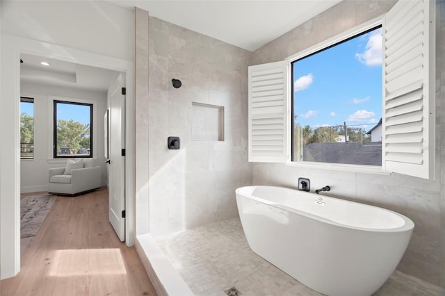 bathroom featuring wood-type flooring, separate shower and tub, and tile walls