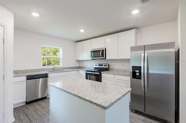 kitchen with stainless steel appliances, a kitchen island, sink, light hardwood / wood-style flooring, and white cabinetry