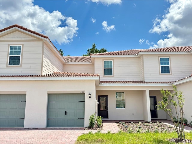 view of front of property featuring a tiled roof, decorative driveway, stucco siding, and a garage