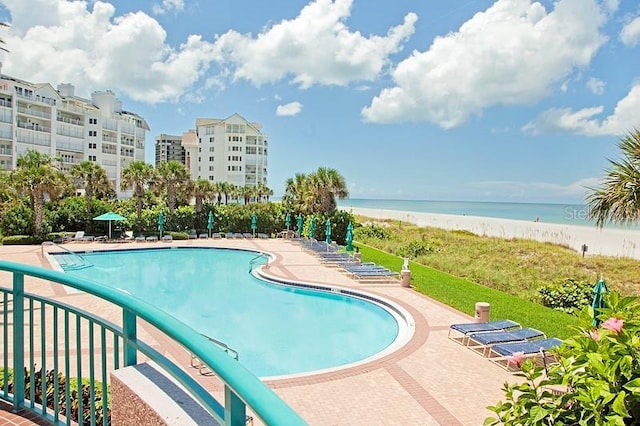 view of pool featuring a water view, a patio, and a view of the beach