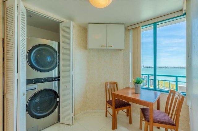 clothes washing area featuring a water view, a healthy amount of sunlight, and stacked washer / drying machine