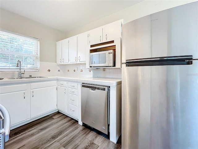 kitchen with appliances with stainless steel finishes, light wood-type flooring, tasteful backsplash, sink, and white cabinetry