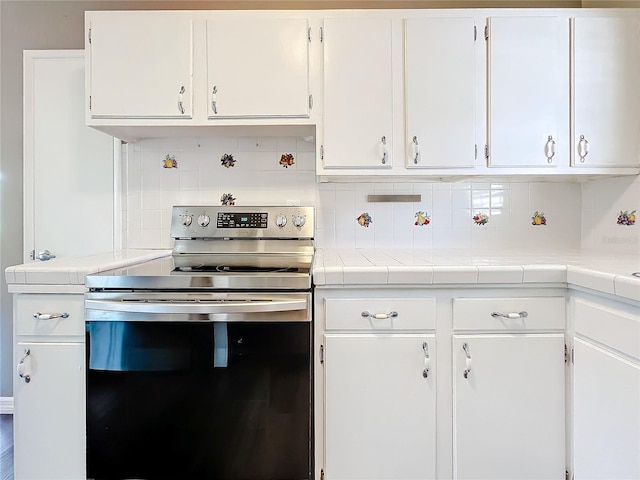 kitchen featuring backsplash, white cabinetry, stainless steel range with electric stovetop, and tile counters