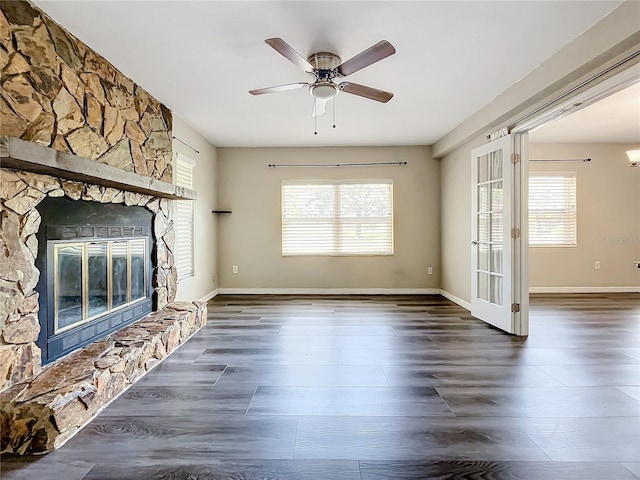 unfurnished living room featuring plenty of natural light, ceiling fan, a fireplace, and dark wood-type flooring