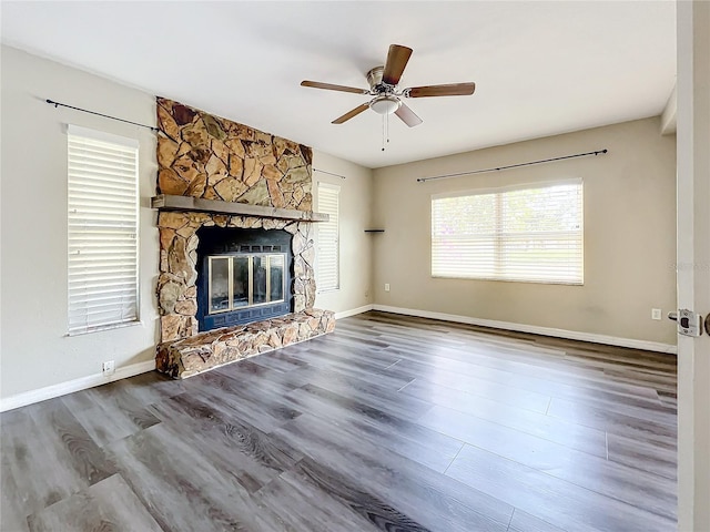 unfurnished living room featuring hardwood / wood-style flooring, ceiling fan, and a stone fireplace