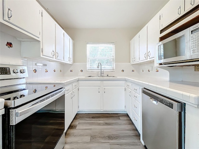 kitchen featuring tile countertops, stainless steel appliances, tasteful backsplash, white cabinetry, and a sink