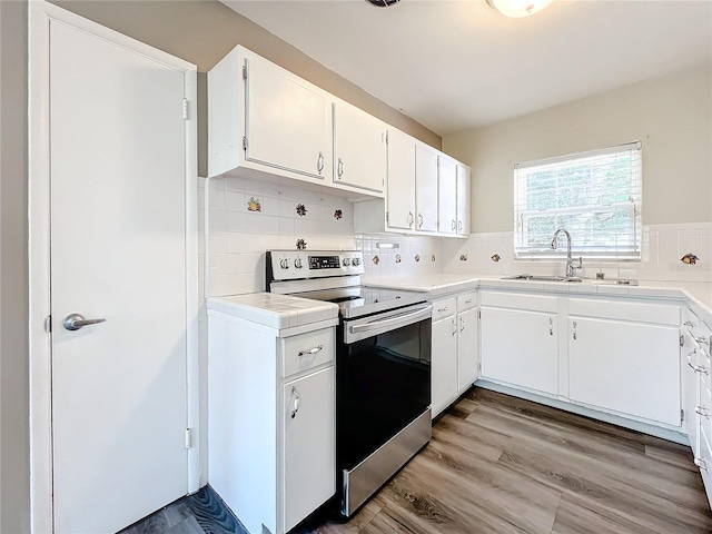 kitchen featuring decorative backsplash, stainless steel electric range oven, light wood-style flooring, white cabinetry, and a sink