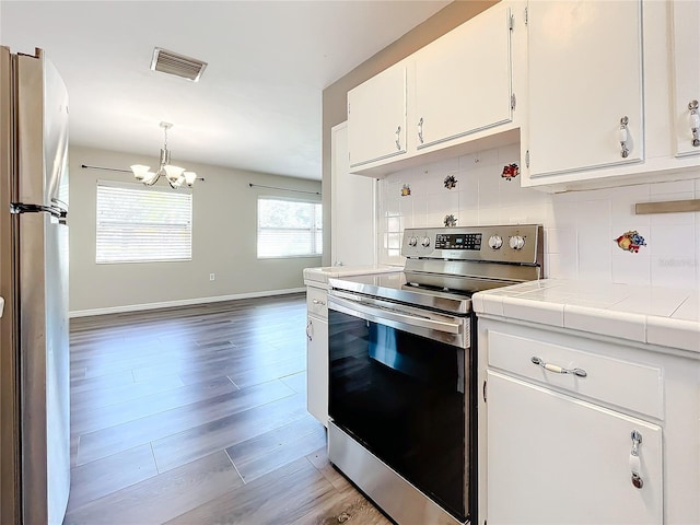 kitchen with tasteful backsplash, visible vents, tile counters, stainless steel appliances, and white cabinetry