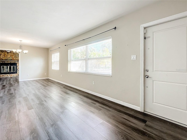 unfurnished living room with an inviting chandelier, a stone fireplace, baseboards, and wood finished floors