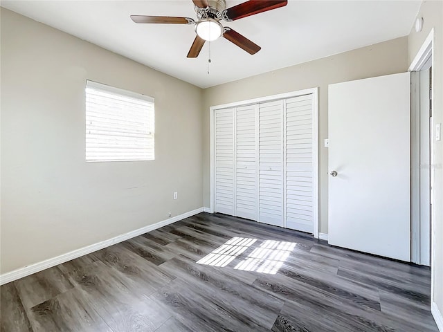 unfurnished bedroom with a ceiling fan, a closet, baseboards, and dark wood-type flooring