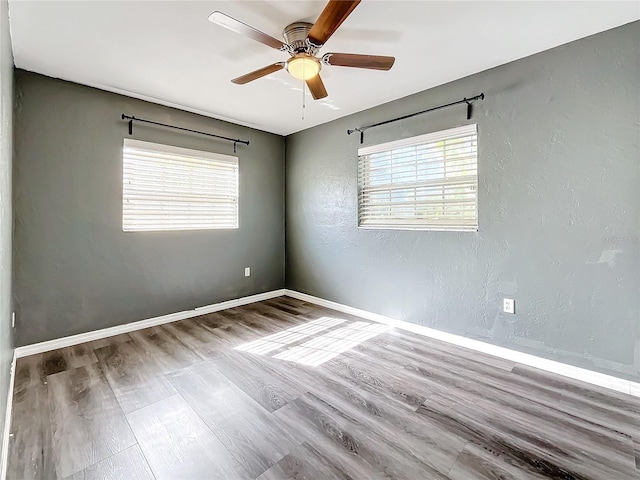 unfurnished room with a wealth of natural light, a textured wall, baseboards, and wood finished floors