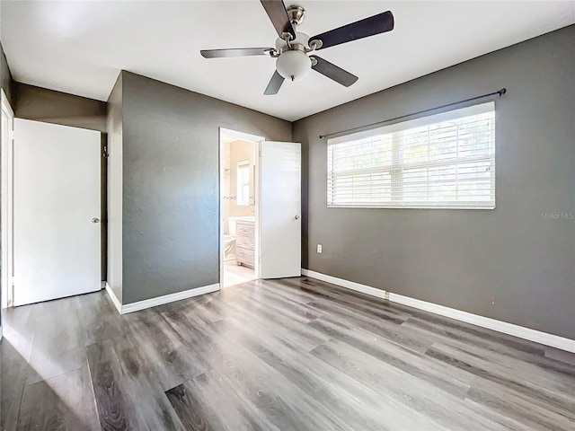 unfurnished bedroom featuring ensuite bath, baseboards, ceiling fan, and wood finished floors