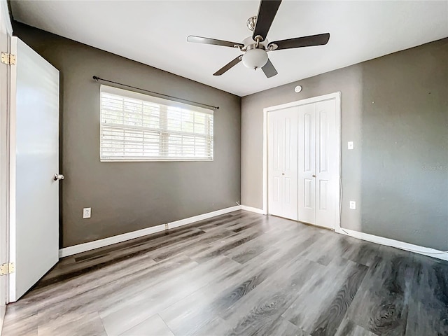 unfurnished bedroom with ceiling fan, a closet, baseboards, and wood finished floors