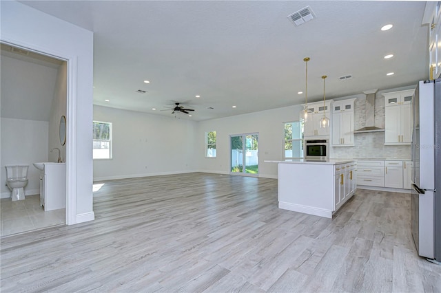 kitchen featuring appliances with stainless steel finishes, wall chimney range hood, light hardwood / wood-style flooring, white cabinets, and plenty of natural light