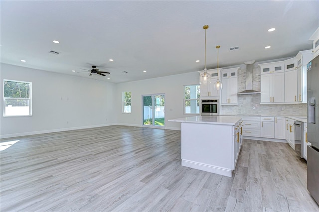 kitchen with a wealth of natural light, white cabinets, and wall chimney range hood