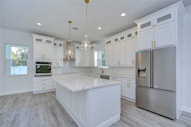 kitchen with a center island, wall chimney range hood, stainless steel appliances, and white cabinetry