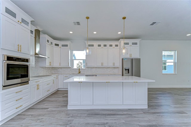 kitchen with a wealth of natural light, a center island, wall chimney range hood, and appliances with stainless steel finishes