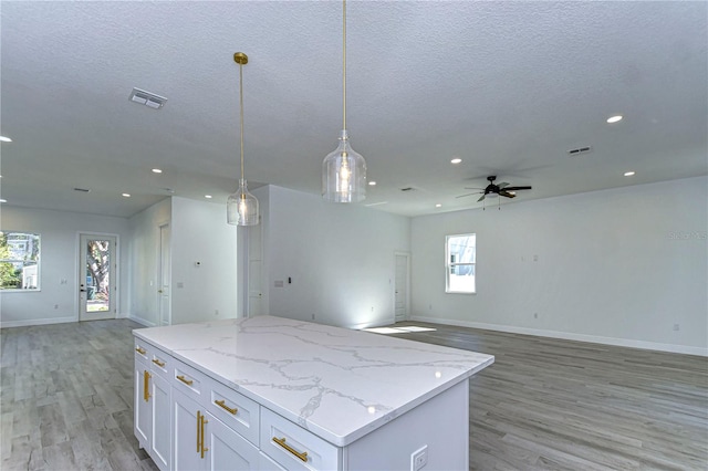 kitchen with pendant lighting, light hardwood / wood-style flooring, ceiling fan, light stone counters, and white cabinetry