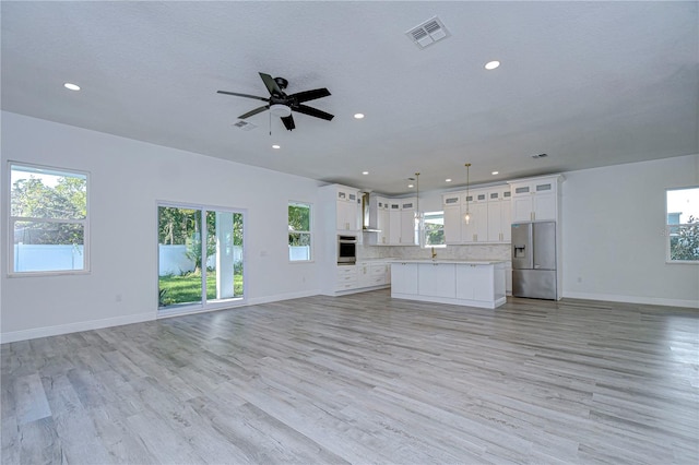 unfurnished living room featuring ceiling fan, light wood-type flooring, and a textured ceiling