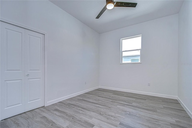 unfurnished bedroom with ceiling fan, a closet, light hardwood / wood-style floors, and lofted ceiling